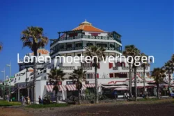 Lonen moeten verhogen op Tenerife - Exotisch hotel met palmbomen onder helderblauwe hemel.